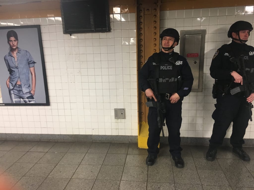 Military-looking police in the subway in New York alongside jeans ad on wall