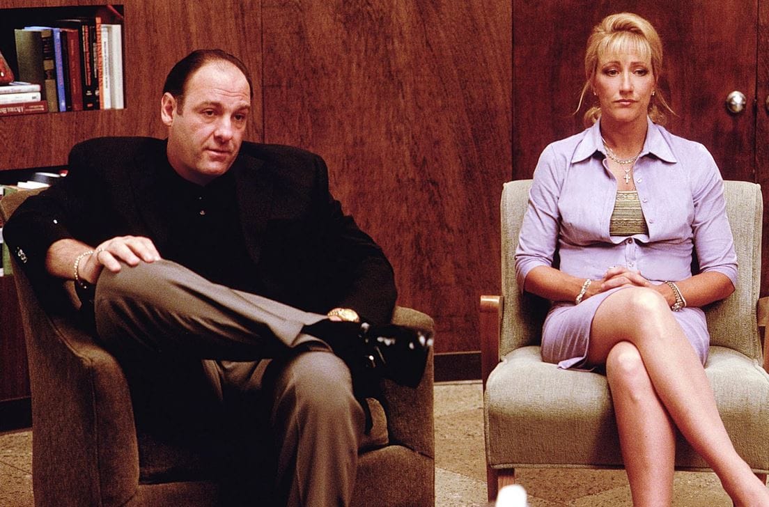 Tony and Carmela Soprano in Dr. Melfi's wood-paneled office, Carmela in a periwinkle shirtwaist and Tony in a dark jacket and taupe trousers.