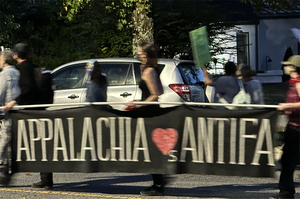 Ladies march, holding a large banner between them reading APPALACHIA <3s ANTIFA