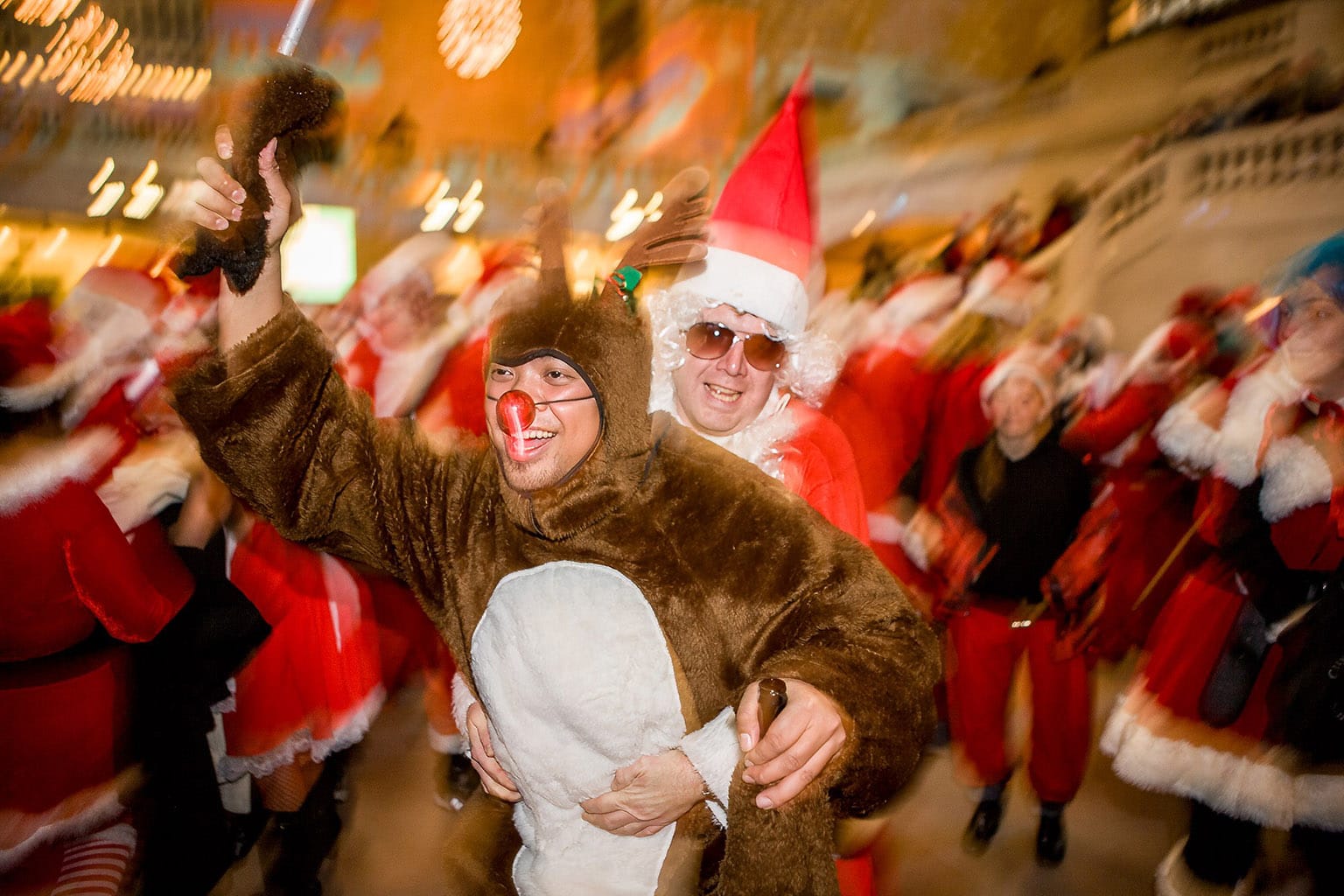 A Santa and a reindeer in the crowd at the train station engaged in a gleeful simulacrum of sexual congress