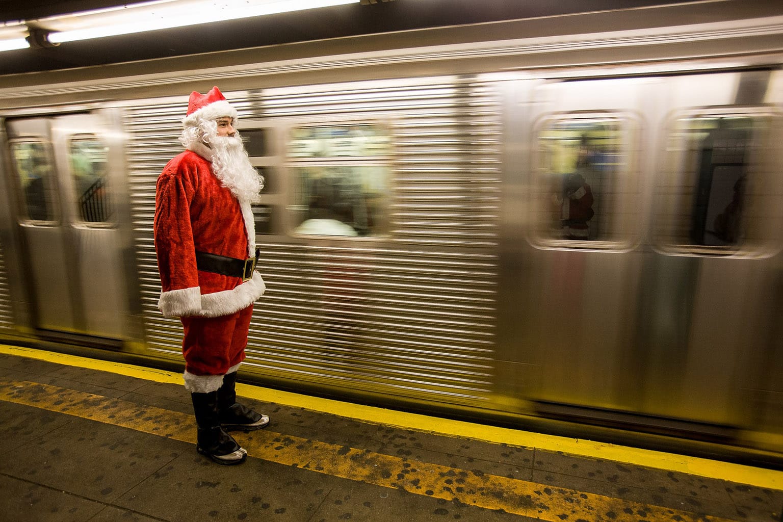 A Santa standing unsafely over the yellow tape as a subway car speeds by