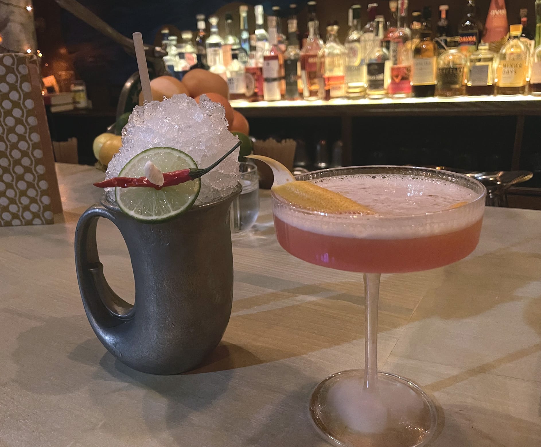 Two incredibly delicious-looking drinks, one in a tankard piled high with crushed ice, the other grapefruit-pink, with a perfectly tender curl of citrus peel atop its foamy surface