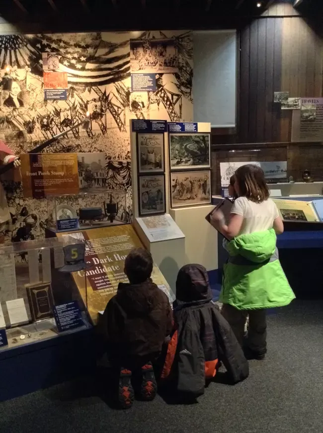 Four young students crowd round to read the captions on museum exhibits, maps, and cases at the Garfield Site in Mentor, Ohio
