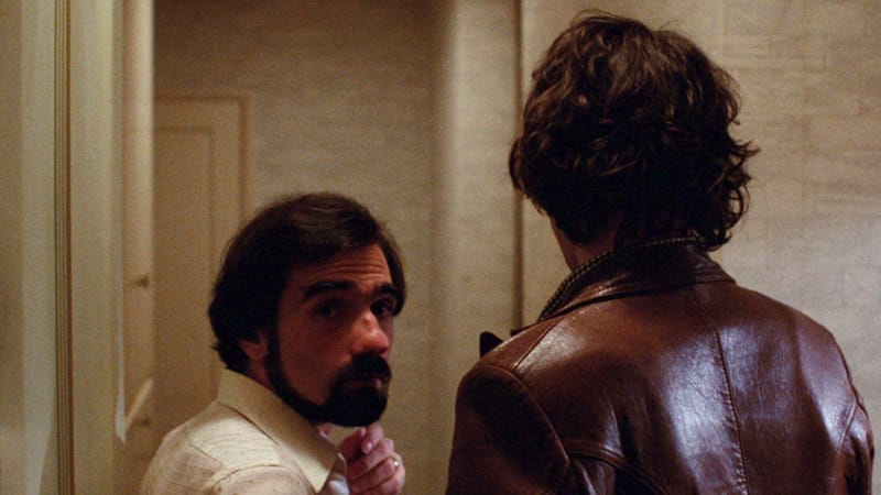 Martin Scorsese, young, bearded, in a beige beige hotel hallway speaking with the much taller Robbie Robertson (brown leather jacket)