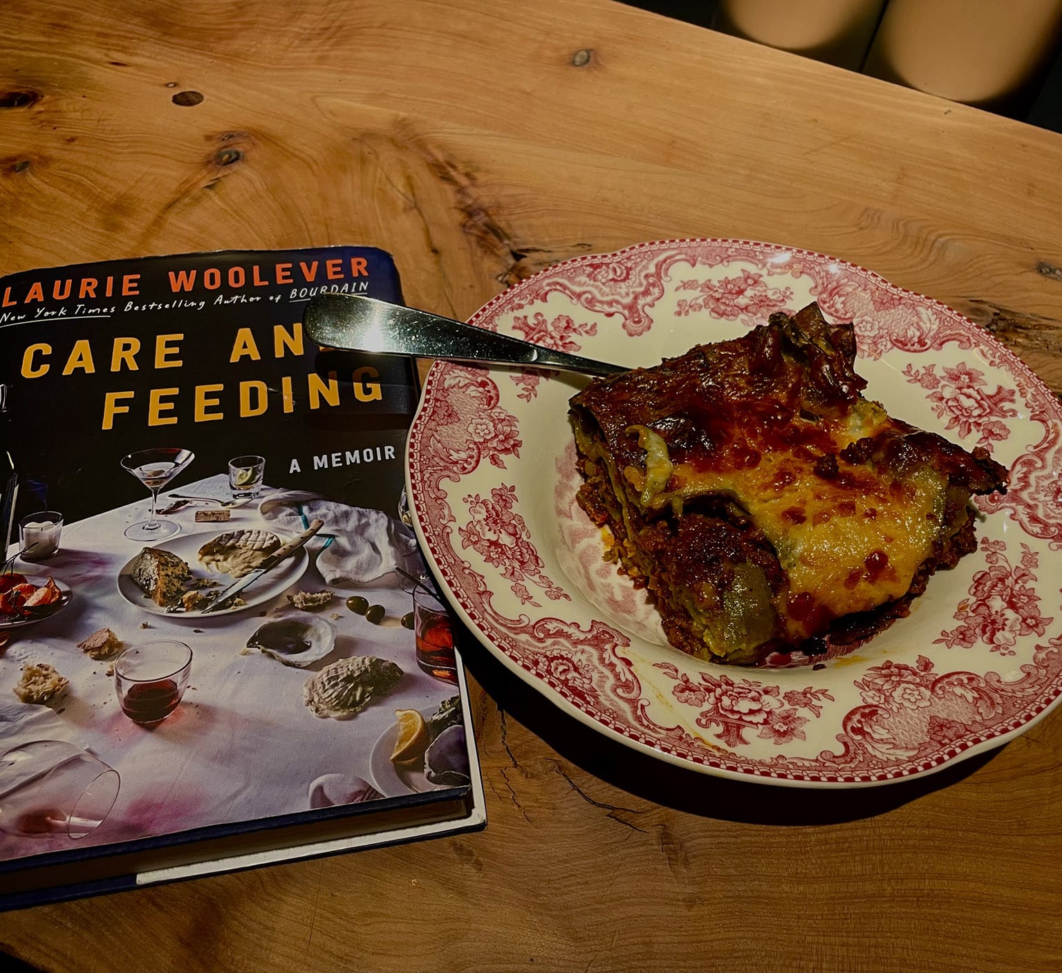 A copy of the author's book, CARE AND FEEDING, and a toile-printed plate with very delicious looking serving of lasagne thereupon 