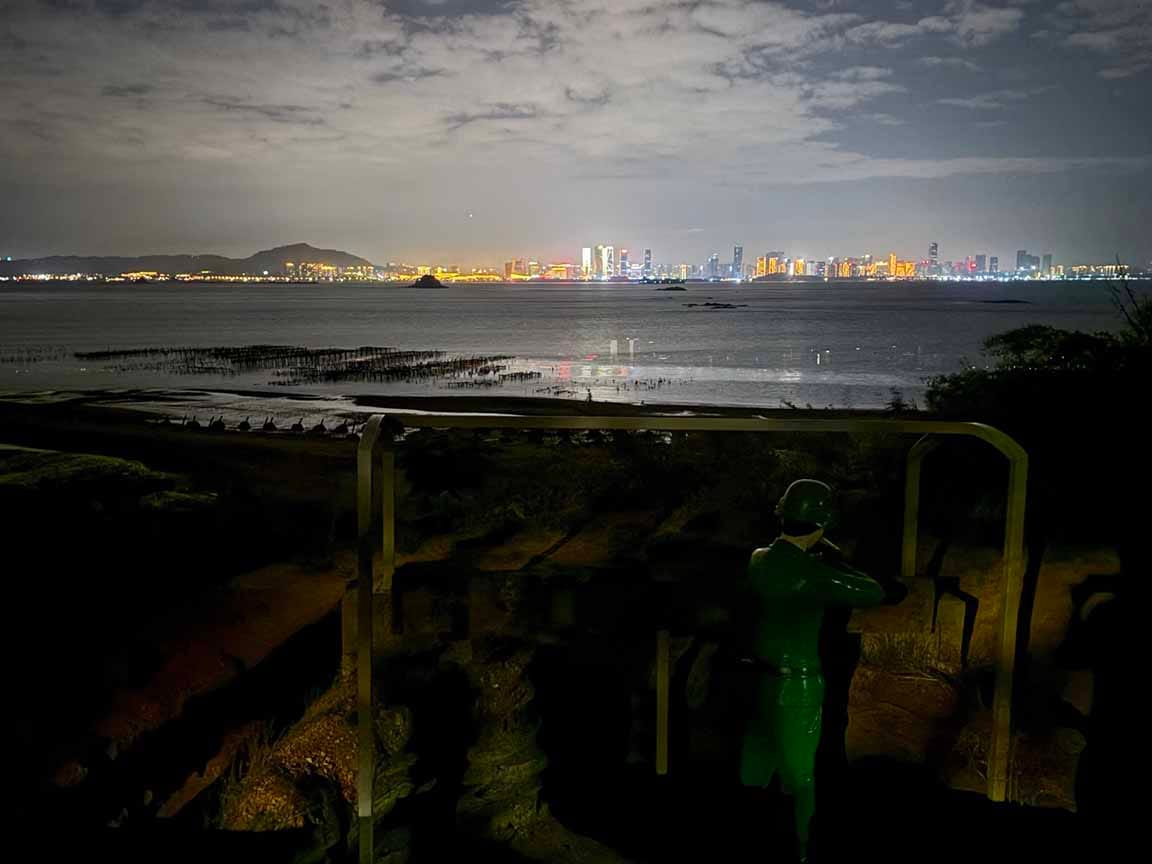 Xiamen, China, as visible from Kinmen’s coast. Statue of a soldier with a rifle pointed at Xiamen in foreground. 