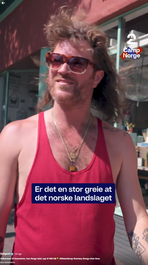 Dude in a red singlet big sunglassses and 70s hairdo with gold chains and Egyptian themed tattoos is interviewed by a Norwegian film crew