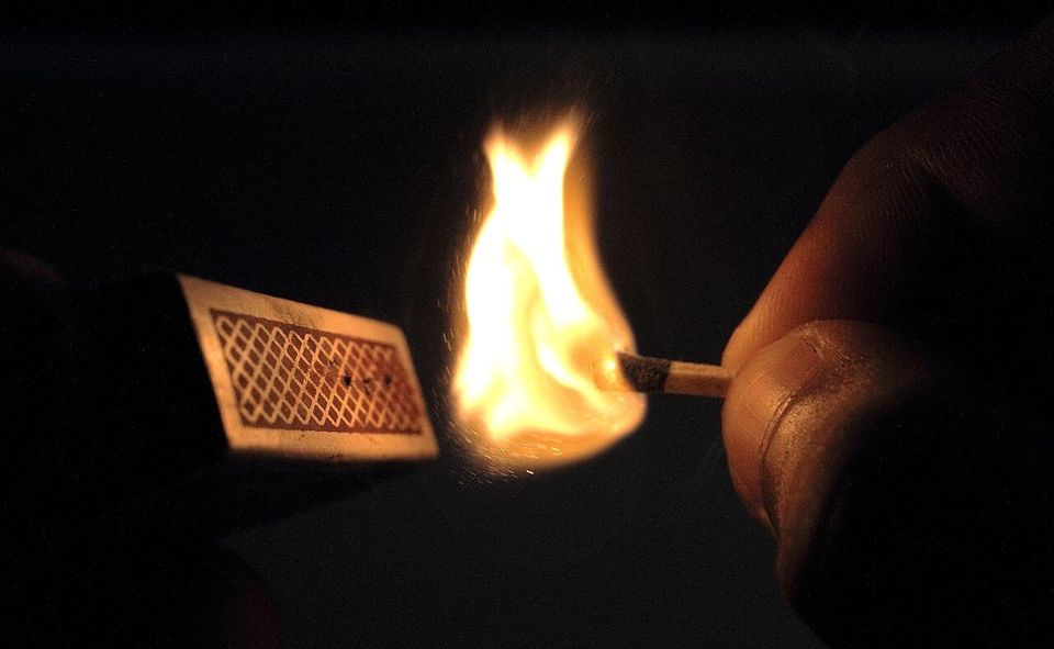 a match as its flame ignites, struck against a matchbox