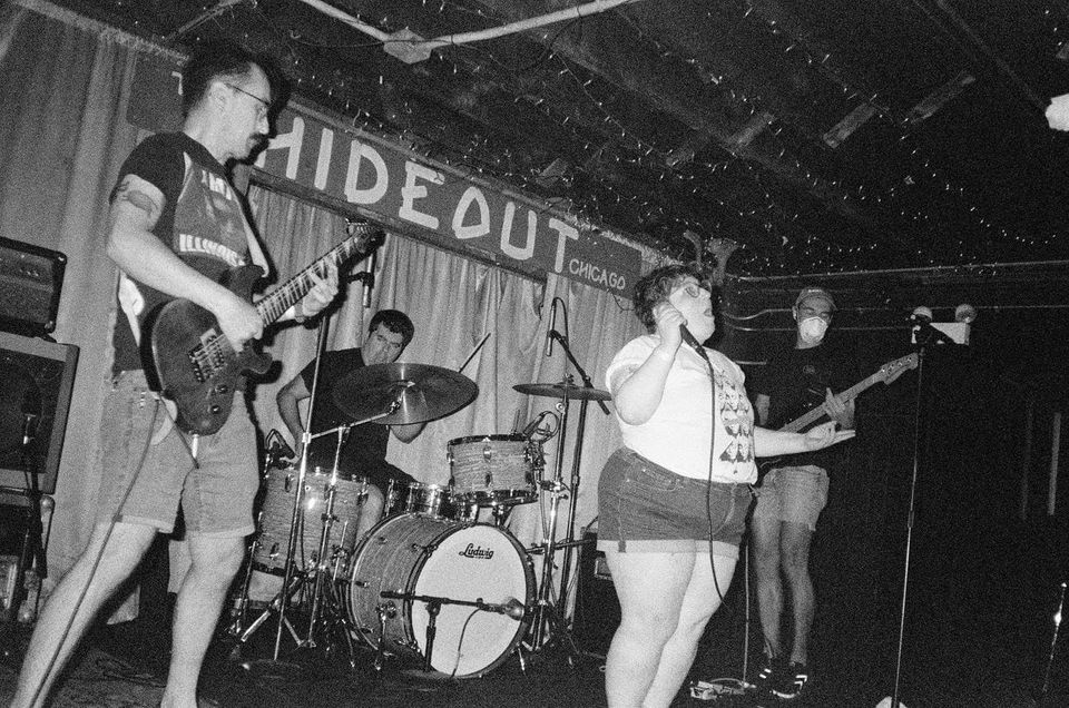 jj on stage with a guitarist, bassist, and drummer, mid-song. A sign above them reads: The Hideout, Chicago. 