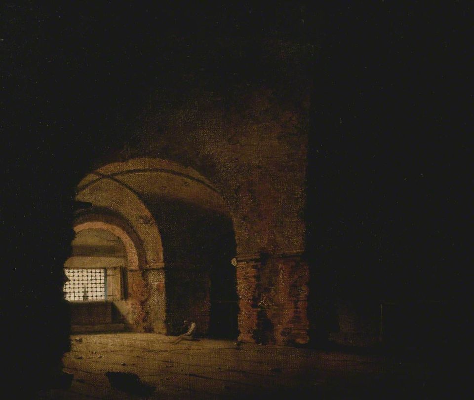 A lone figure, head bowed, seated on the floor of a dark prison cell with light filtering in through barred windows