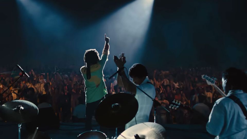 From the film 'One Love', Bob Marley in the spotlight, one arm raised, with the Wailers on a darkened stage