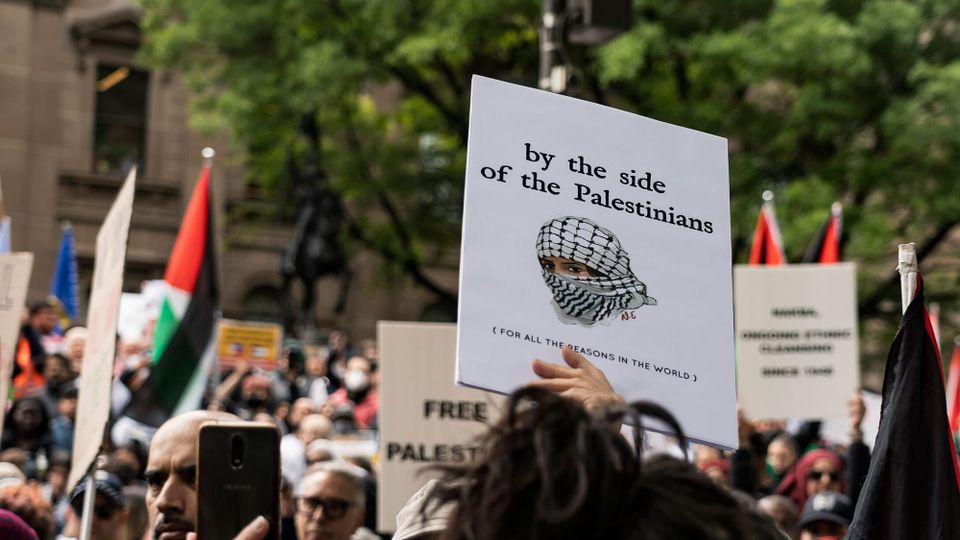 A big October 2023 protest in Melbourne; protester holds a sign reading 'by the side of the Palestinians'