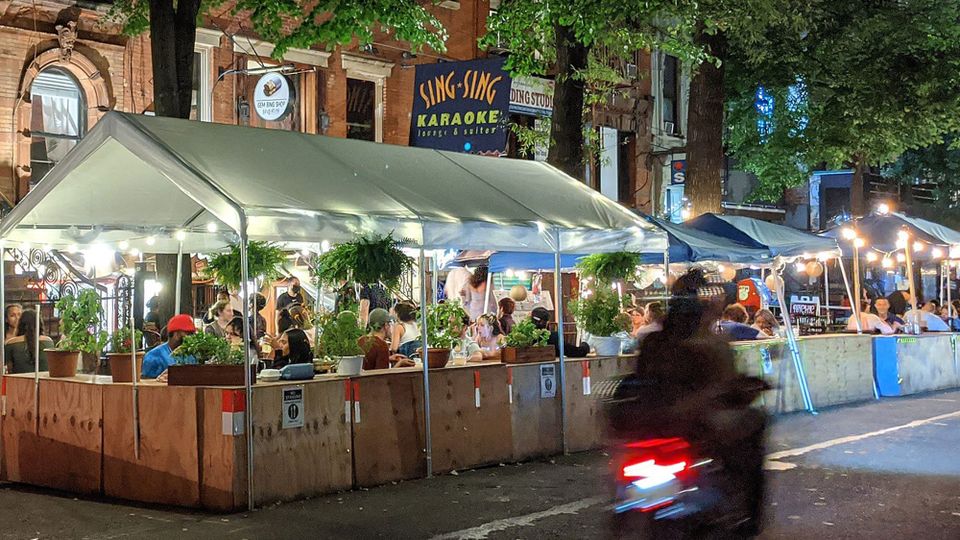 A tree-lined street showing an outdoor dining setup outside the Sing-Sing Karaoke Lounge on St. Mark's