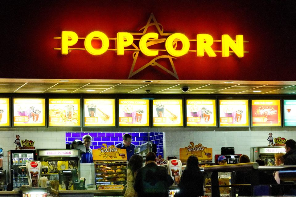 Bright golden 'POPCORN' letters on a red wall above movie theater concession stand