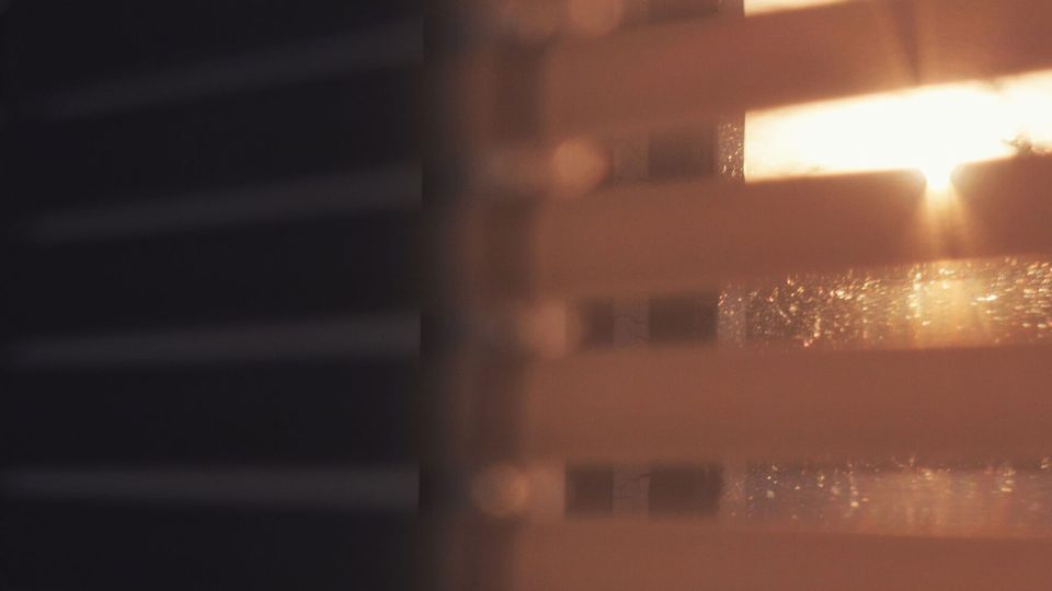 Sepia-toned image of the setting sun coming into a darkened room through half-closed window blinds