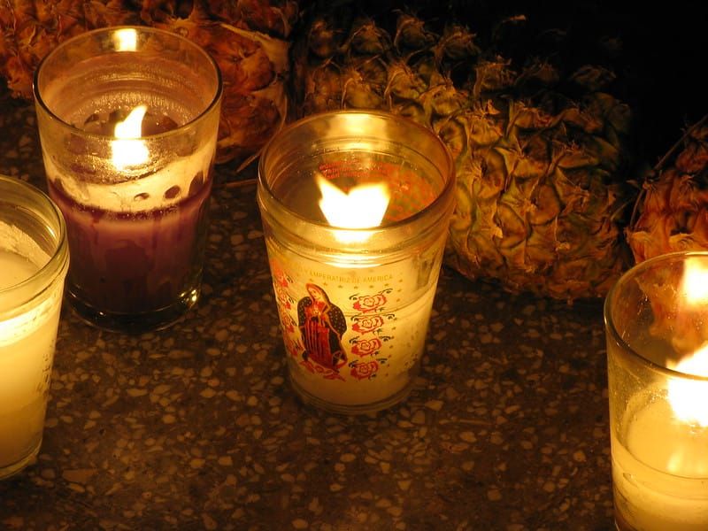 Votives lit before a row of pineapples, the central one a veladora of la Virgen de Guadalupe
