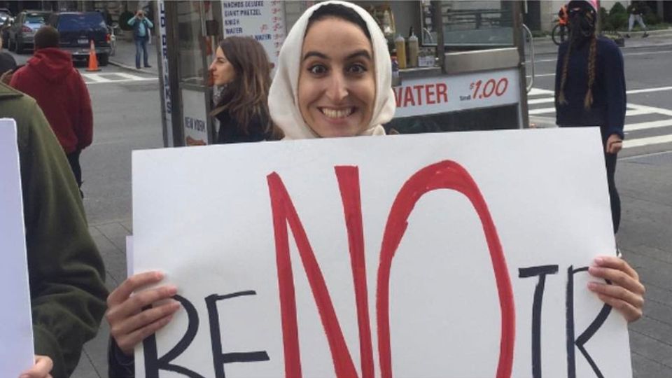 A smiling woman holding up a large black and white sign reading, "reNOir"