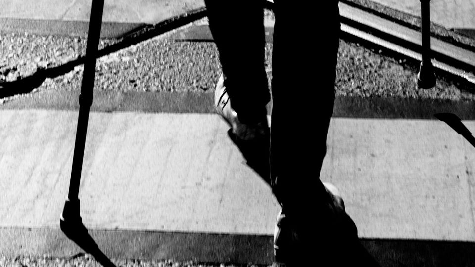 Detail from a black and white photo of someone on crutches, walking away, just from the knees down