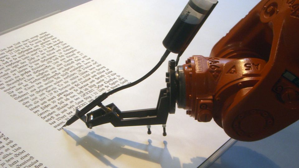 A red metal robot arm with an ink canister attached, writing on a large white paper