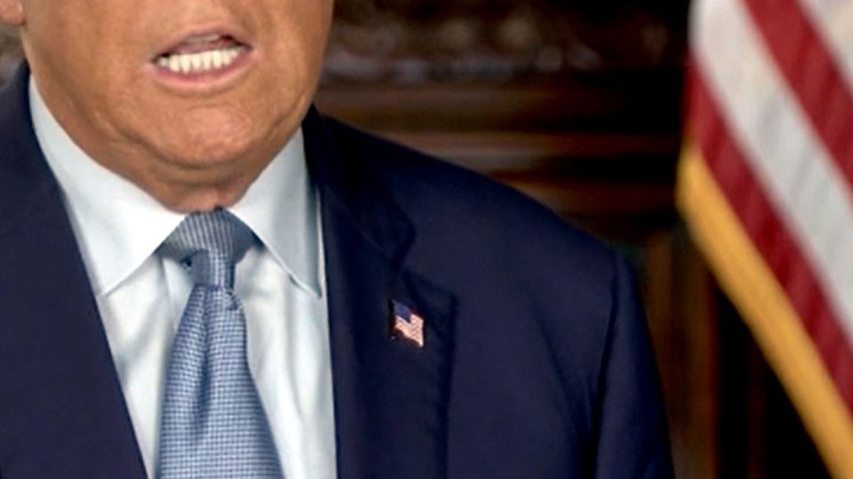 Screenshot of Donald Trump's mouth; also visible,his navy suit and blue tie; there is a tiny flag pin on his lapel