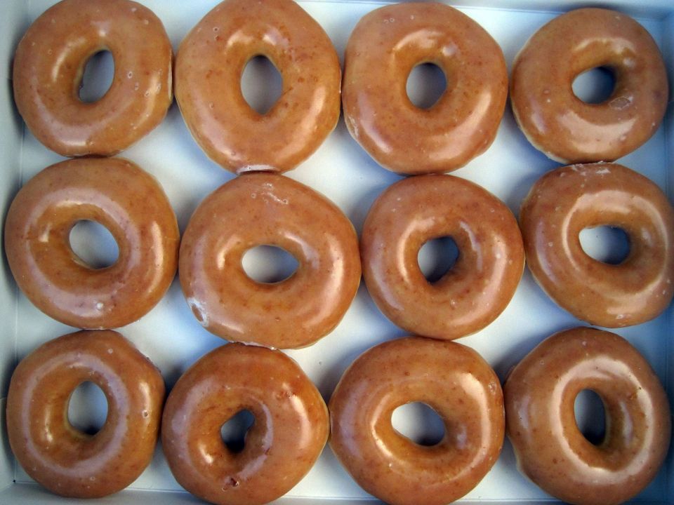 Twelve glossy, luscious looking regular glazed Krispy Kreme donuts in the standard white paper box