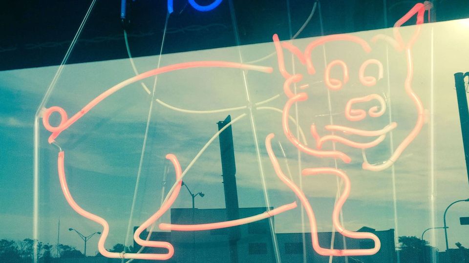 Seen through the window of a restaurant: a pig rendered in bright pink neon