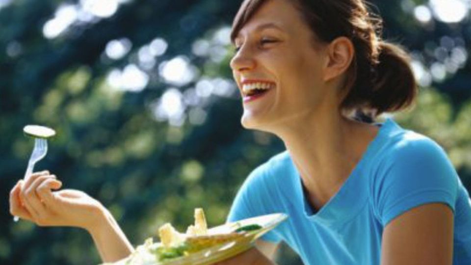 Ponytailed Woman in a blue t-shirt, Laughing, as she spears a bit of cucumber from a Salad