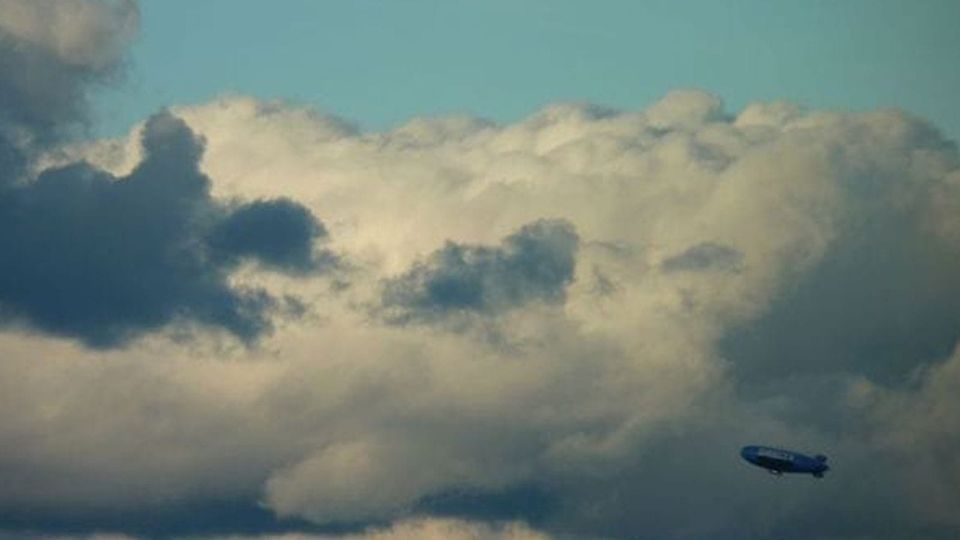 A distant blimp visible against thick clouds, with a rich turquoise sky above