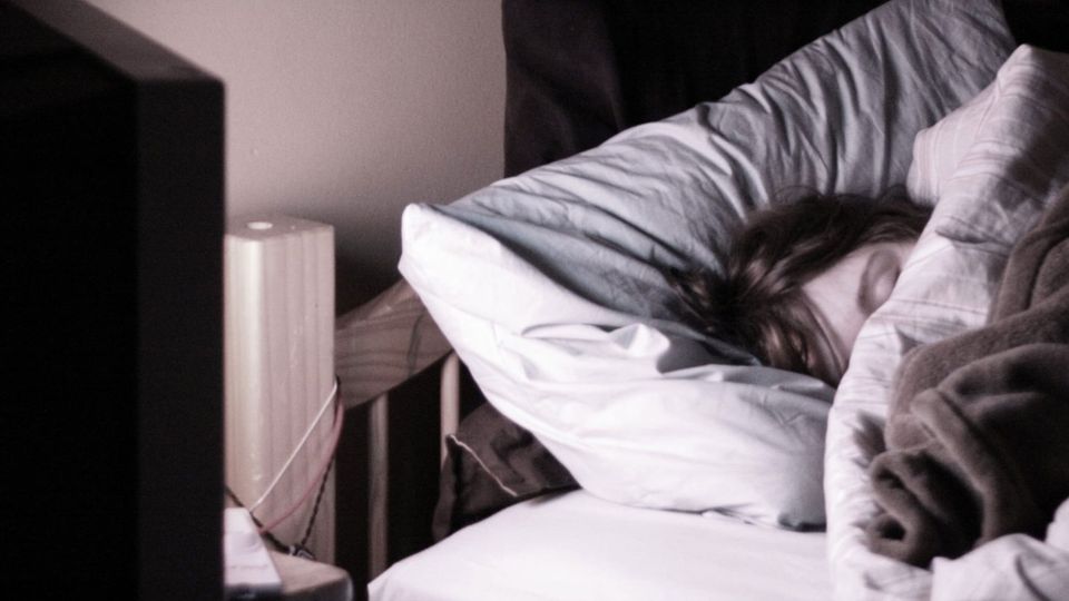 Someone asleep in bed in the glow of a television that is still on