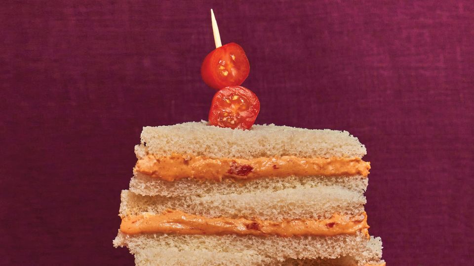 A stack of party sandwich triangles on white bread, garnished with cherry tomatoes