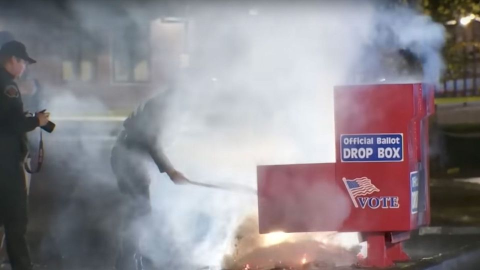 Fireman rakes burning ballots out of a sabotaged drop box in Washington State, October 2024