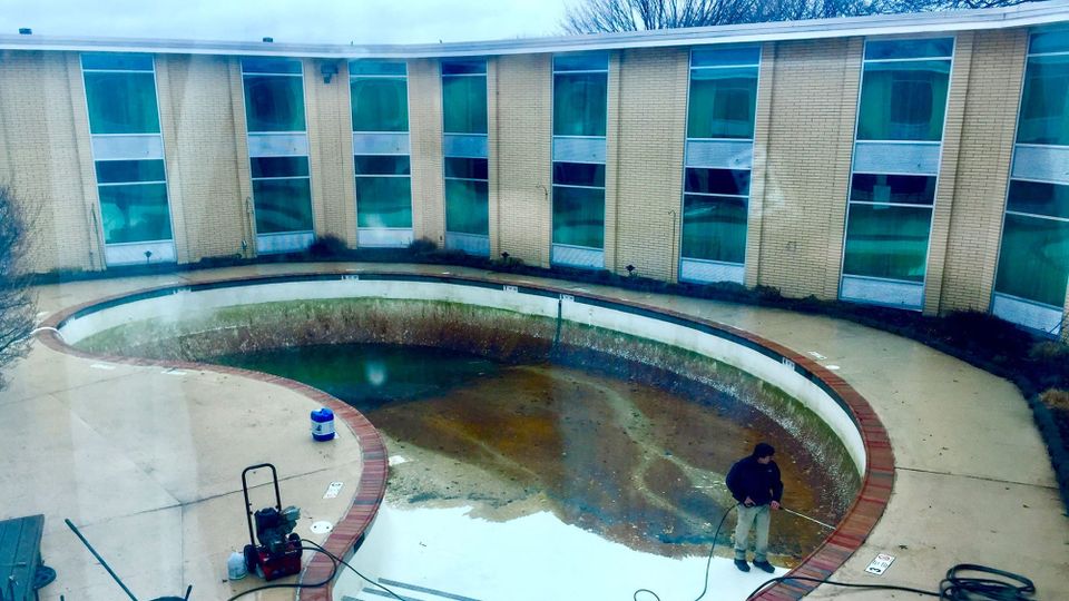 A squat-two story motel with a murky, algae-choked dirty swimming pool, undergoing a cleaning