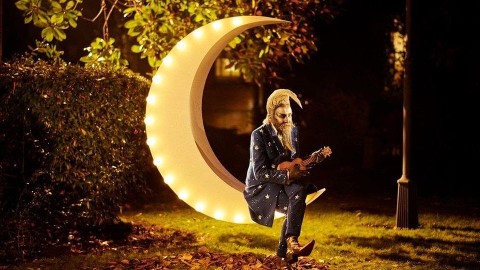 Alan Moore as Frank Metterton in 'The Show', playing a ukelele and seated outdoors on an illuminated moon
