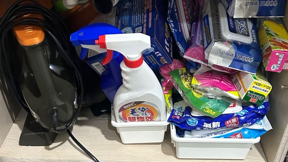 A cabinet filled with plastic containers of cleaning supplies in spray bottles and plastic packaging