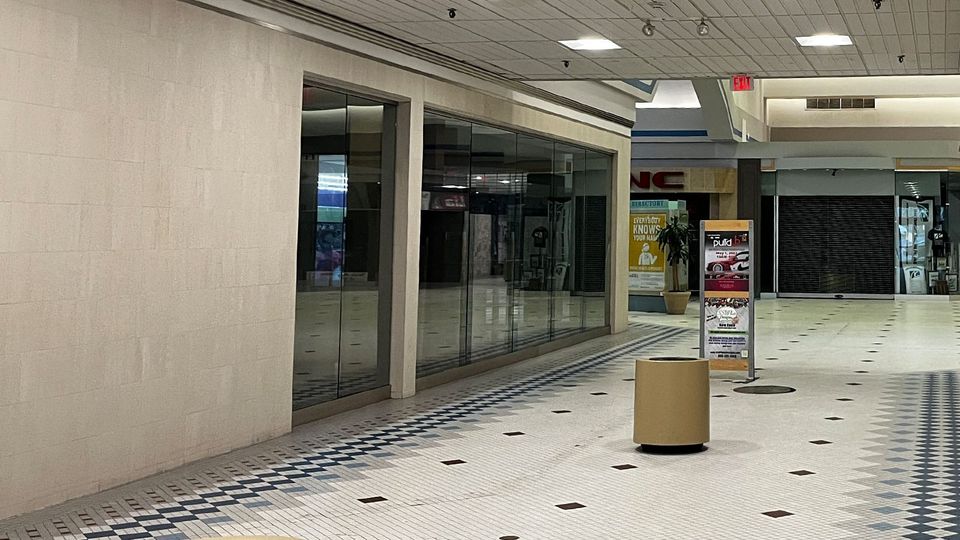 Interior of a dead mall, with beige tile, darkened shops and fluorescent lights