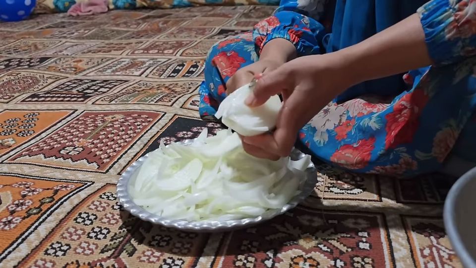 A woman in a blue floral dress, neatly slicing onions into an aluminum dish