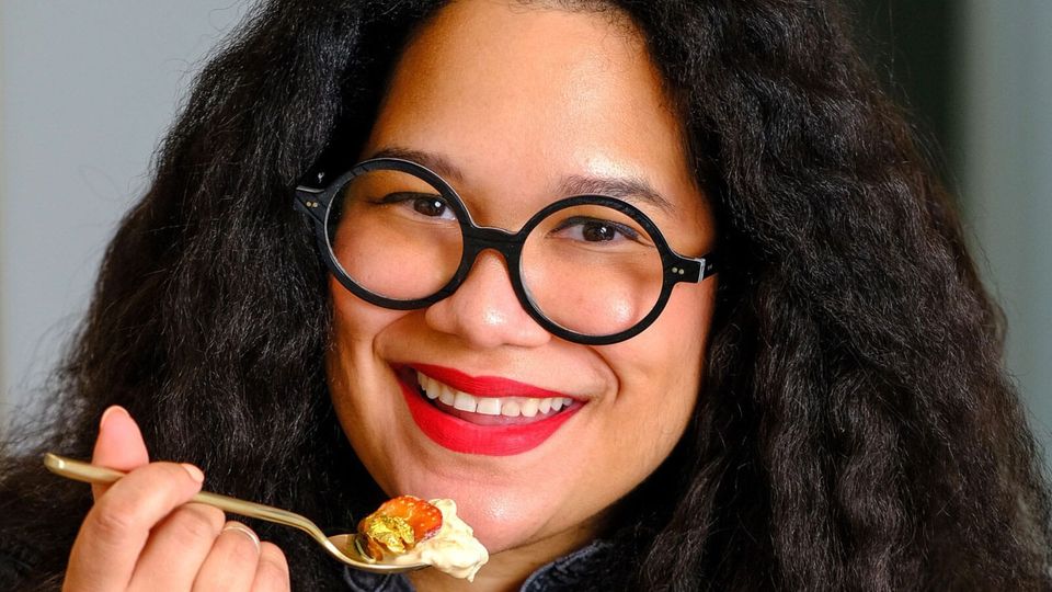 Paola Velez in bright red lipstick and cute round glasses, holding a spoonful of something delicious