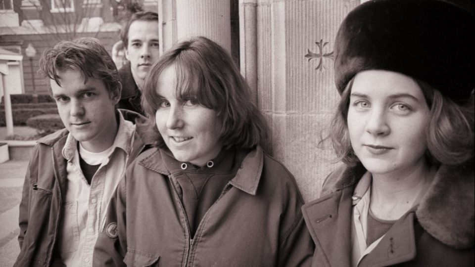 The four members of Tsunami, dressed for cold weather and posing against the corner of a building