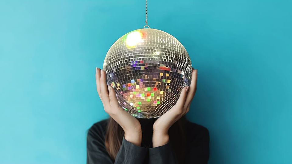 Photo illustration:Person holding their head in their hands but their head is a disco mirror ball.