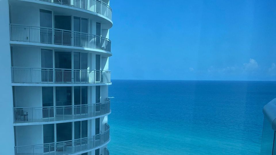 A filmy blue scene in Miami, showing upper floors of a high-rise beachfront hotel against the impossibly sapphire sea