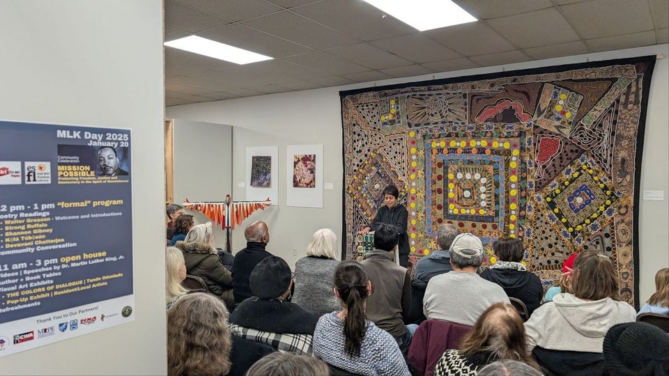 Community celebration on January 20 2025 with speaker reading at podium before a huge, colorful quilt