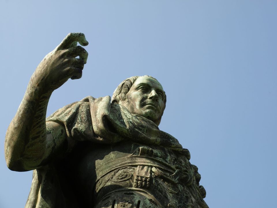 Bronze Roman statue of Julius Caesar, in Turin, Italy, viewed from a low angle with flat dull blue sky above.
