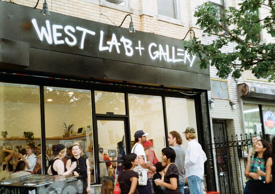 People festively congregating on both sides of gallery's glass storefront.