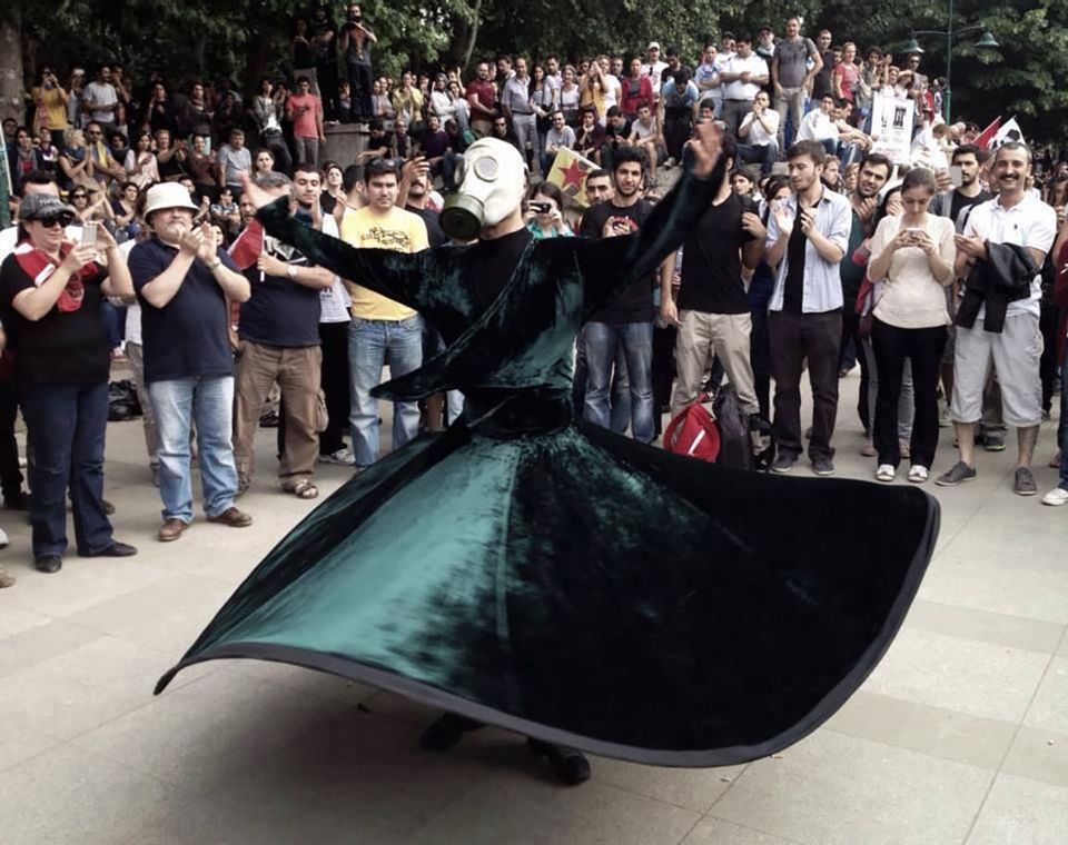 Crowd encouraging whirler who is wearing emerald green garment and a white gas mask