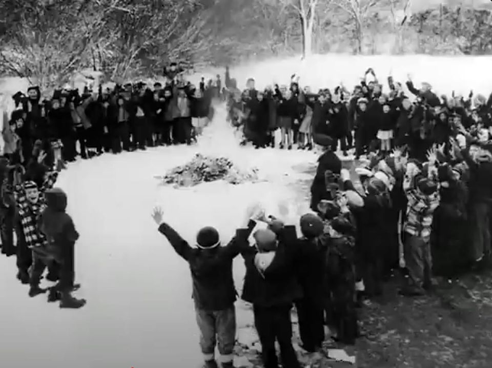 A b&w image of a circle of children cheering as a pile of comic books and magazines burn