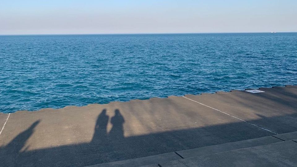 Chicago by the lake in filmy light on a sunny day; the shadows of two people appear on the boardwalk, at some distance