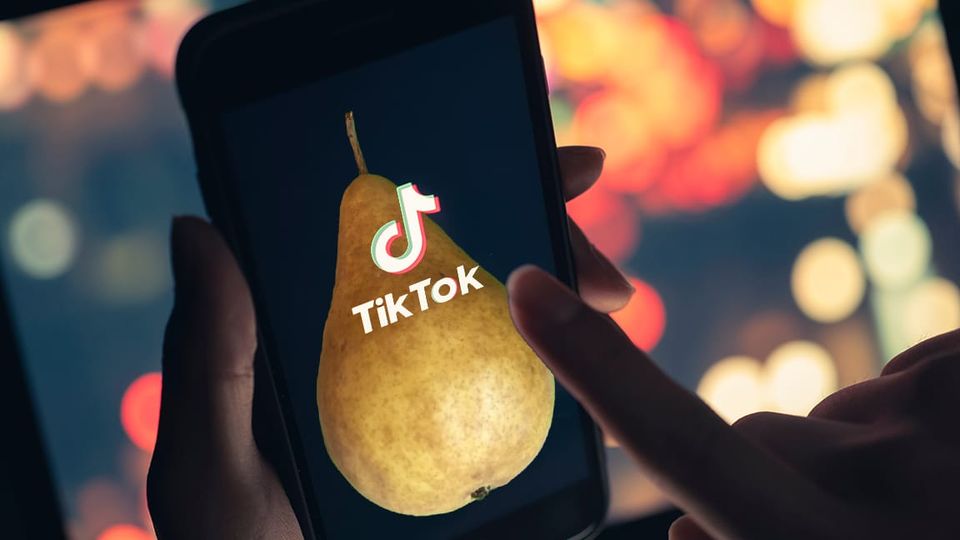 Hands holding phone with image of a pear behind Tik Tok logo