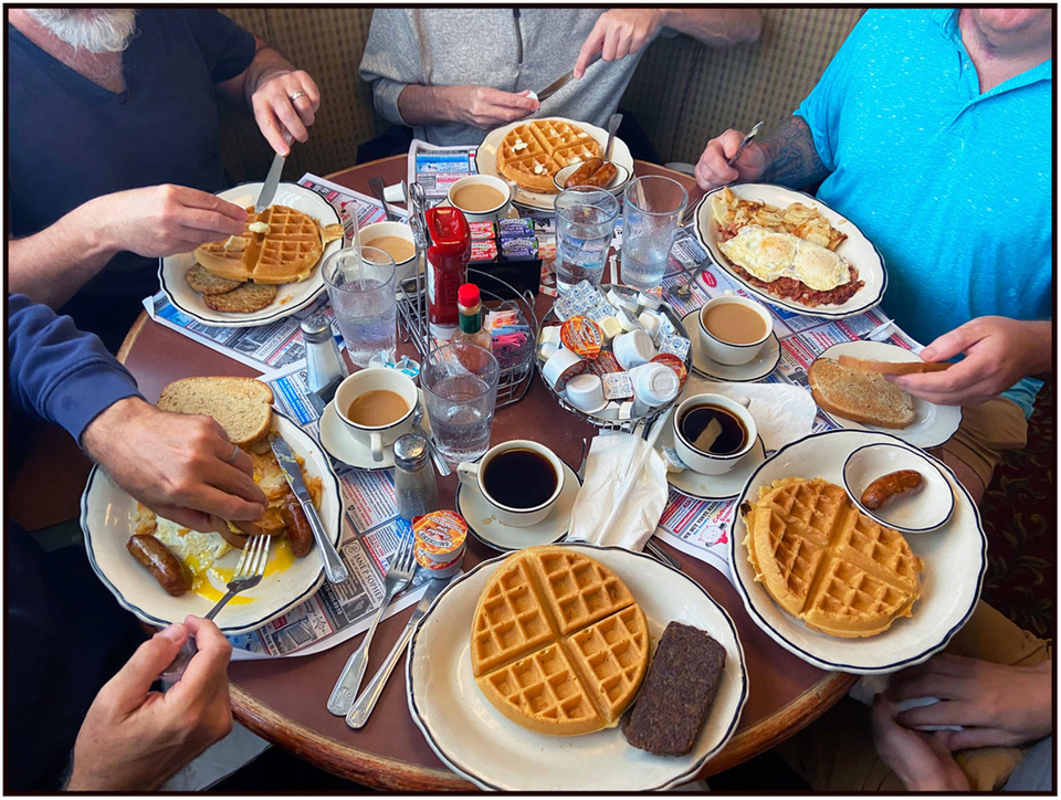 A table of breakfasters enjoying waffles, eggs, home fries, bacon, sausage, scrapple, toast and coffee