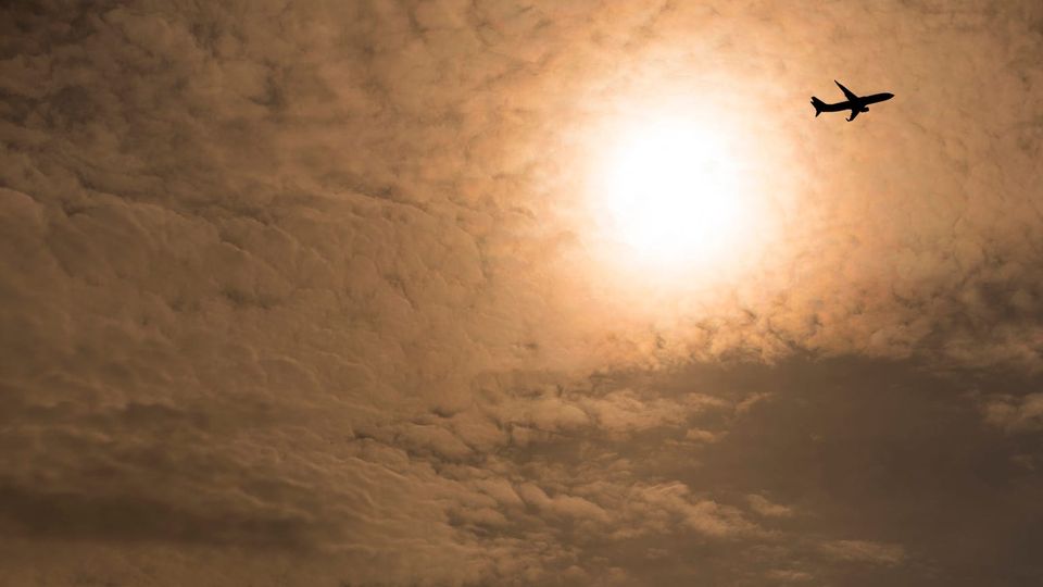 Hazy warm darkening sky with diffuse sun and a plane flying away