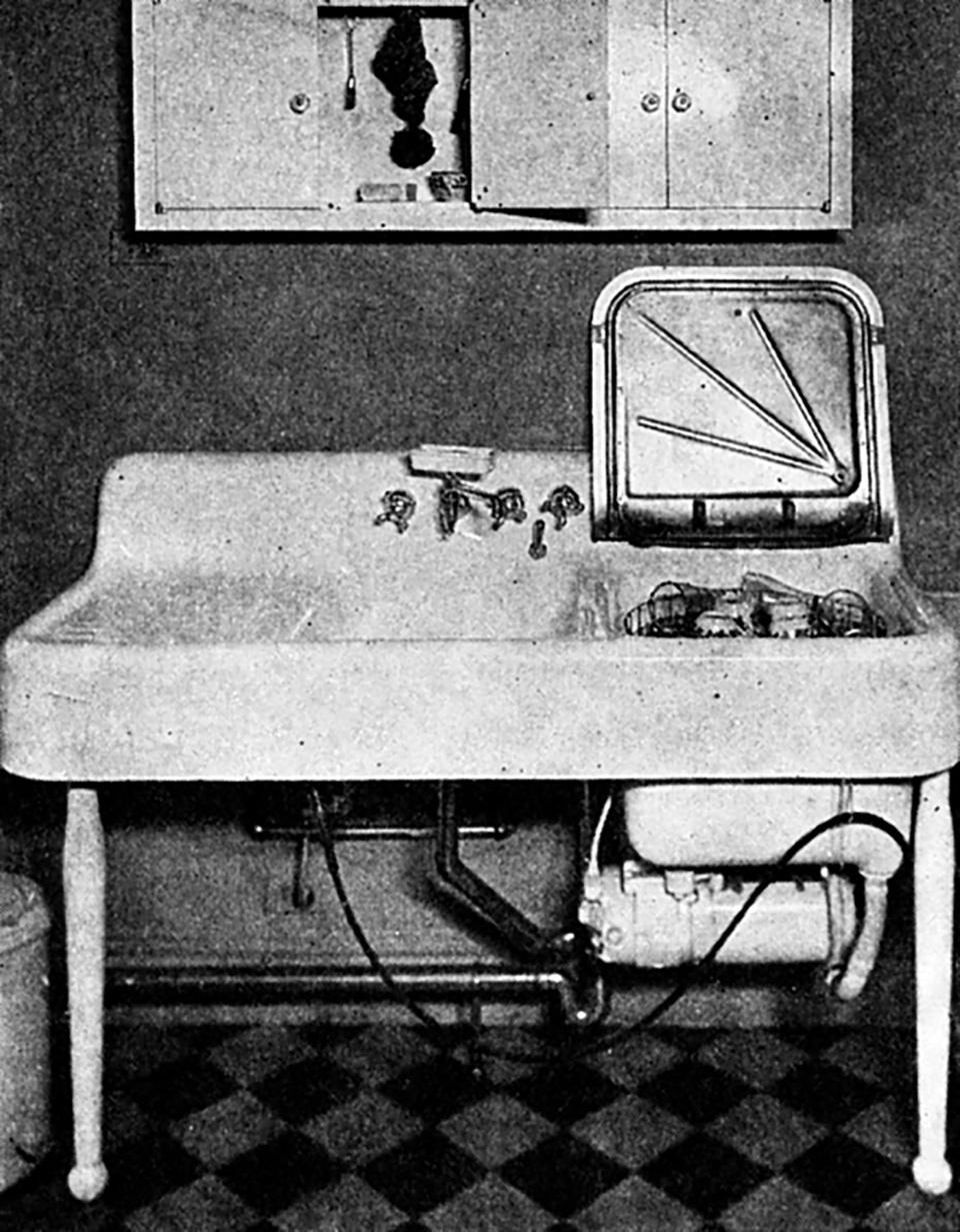 An ancient, grimy, and depressing automatic dishwasher setup installed onto a large white enamel cast iron sink.